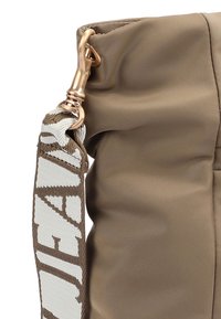 Primo piano di una borsa in tessuto marrone con una chiusura dorata e una tracolla a fantasia bianca e marrone.