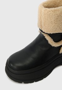 Μαύρη δερμάτινη μπότες με κρεμ faux-shearling μανσέτα, χοντρή μαύρη πλατφόρμα και καμπυλωτό σχέδιο για επιπλέον στήριξη και άνεση.
