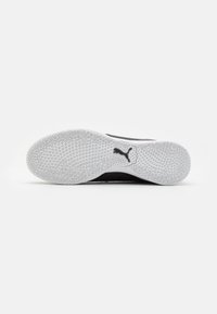 Suela de zapato deportivo negro con patrones de tracción circulares, ligera, con una entresuela blanca y un logo negro en el talón.