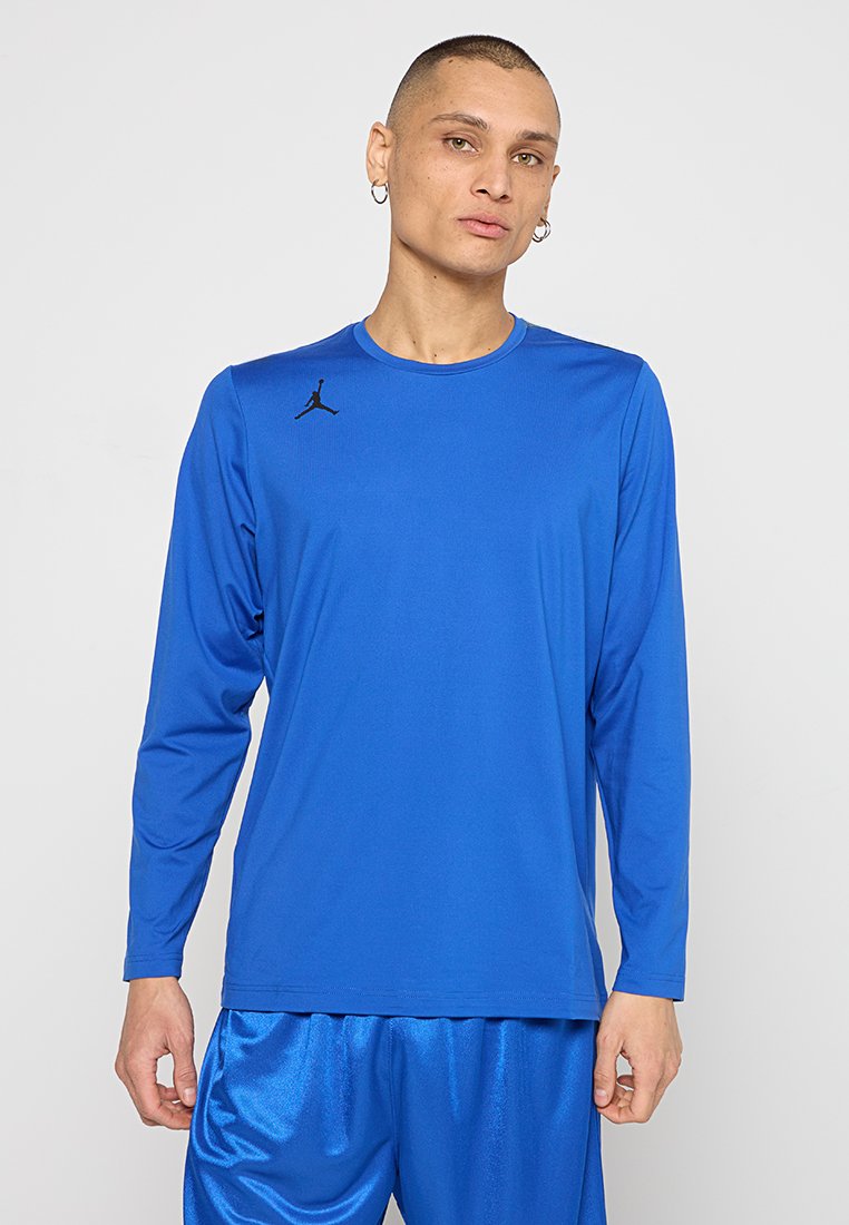 T-shirt de sport à manches longues en bleu vif, fabriqué en matériau synthétique lisse, avec un logo Jumpman noir sur la poitrine.