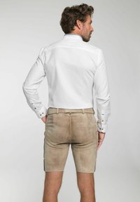 Weißes Langarmhemd mit strukturiertem Design und blauen Nähten am Kragen, kombiniert mit beigen Shorts aus weichem Material.