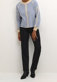 Pull rayé bleu et beige avec un col rond et des poignets côtelés, associé à un jean noir à jambes droites et des bottines noires épaisses.