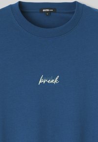 T-shirt bleu col rond à coupe ample avec texte blanc brodé "break" centré sur la poitrine, taille large avec étiquette de la marque BZB à l'intérieur du col.