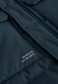 Material textil bleumarin cu o textură netedă, având o etichetă cu text alb: "GB/45/2/78 LOT 161.LDN 01" pe o secțiune pliată.