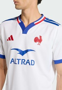 Bílé fotbalové dres Adidas s modrými akcenty, výstřihem do V a červeným emblémem kohouta. Pod kohoutem modré logo "ALTRAD".