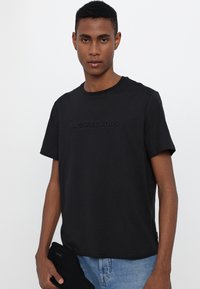 Camiseta de algodón negra con cuello redondo y mangas cortas, con el logotipo en relieve "MICHAEL KORS" en el pecho.