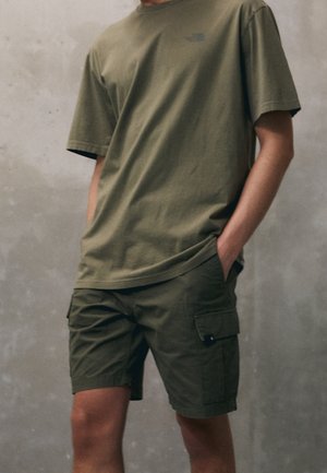 T-shirt olive avec un col rond et des manches courtes, associé à un short cargo olive avec des poches latérales. Design minimaliste.