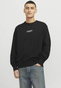 Sudadera negra con cuello redondo y puños acanalados, que presenta un logotipo de texto en blanco "ICONIC" en el pecho. Material de algodón, corte relajado.
