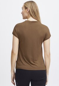 Brun kortærmet t-shirt med en glat tekstur, rund halsudskæring og en afslappet pasform, parret med sorte bukser, set fra ryggen.