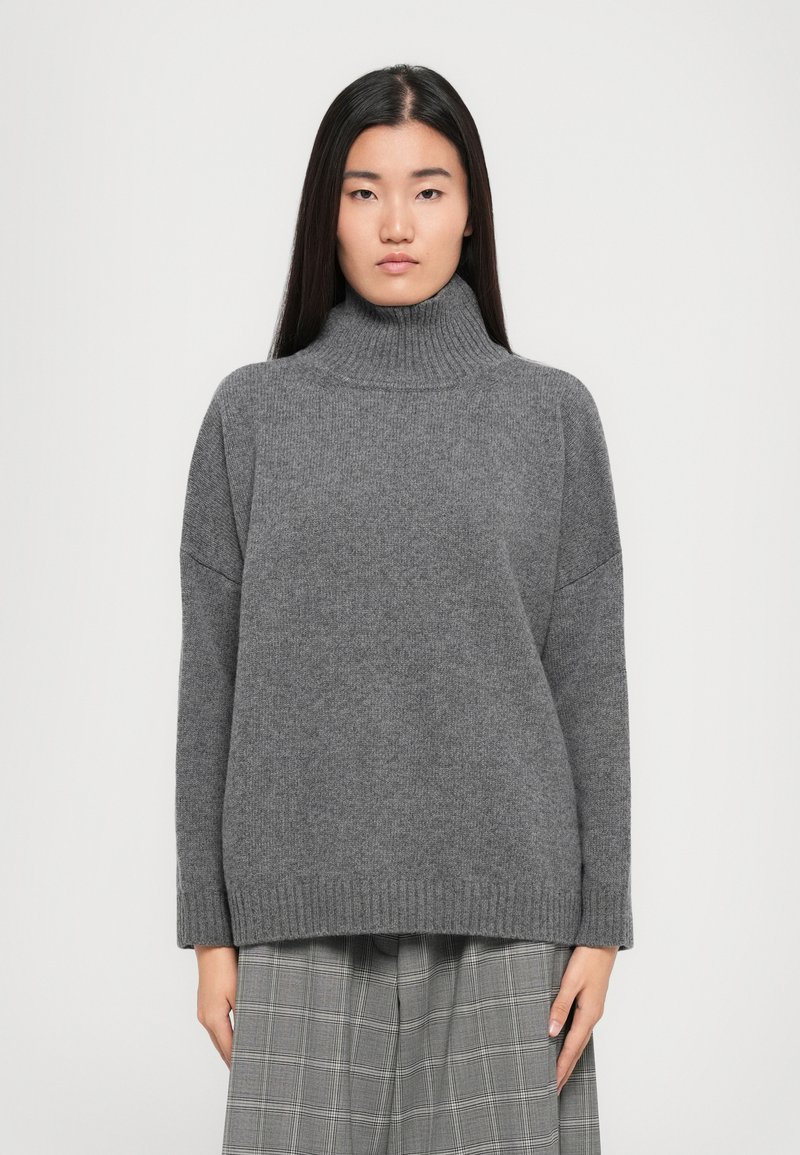 Grauer Rollkragenpullover aus Strickstoff, mit lässiger Passform, geripptem Kragen und Saum, kombiniert mit karierten Hosen.