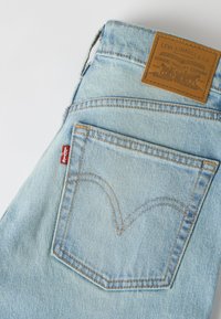 Φωτεινά γαλάζια τζιν παντελόνια με ορατή πίσω τσέπη, κόκκινη ετικέτα Levi's και καφέ δερμάτινη ετικέτα της μάρκας Levi Strauss & Co. στη μέση.