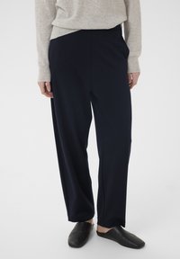 Marineblå vidde bukser lavet af blødt stof med en afslappet pasform og sidelommer, kombineret med sorte slip-on sko.