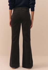 Pantaloni a zampa in velluto di cotone nero con una finitura testurizzata, dotati di due tasche posteriori e una vita media, caratterizzati da una leggera svasatura all'orlo.