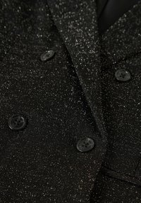 Czarna, dwurzędowa marynarka z teksturowanej, błyszczącej tkaniny. Posiada czarne guziki i klapę ze szczeliną, prezentując błyszczący wygląd.