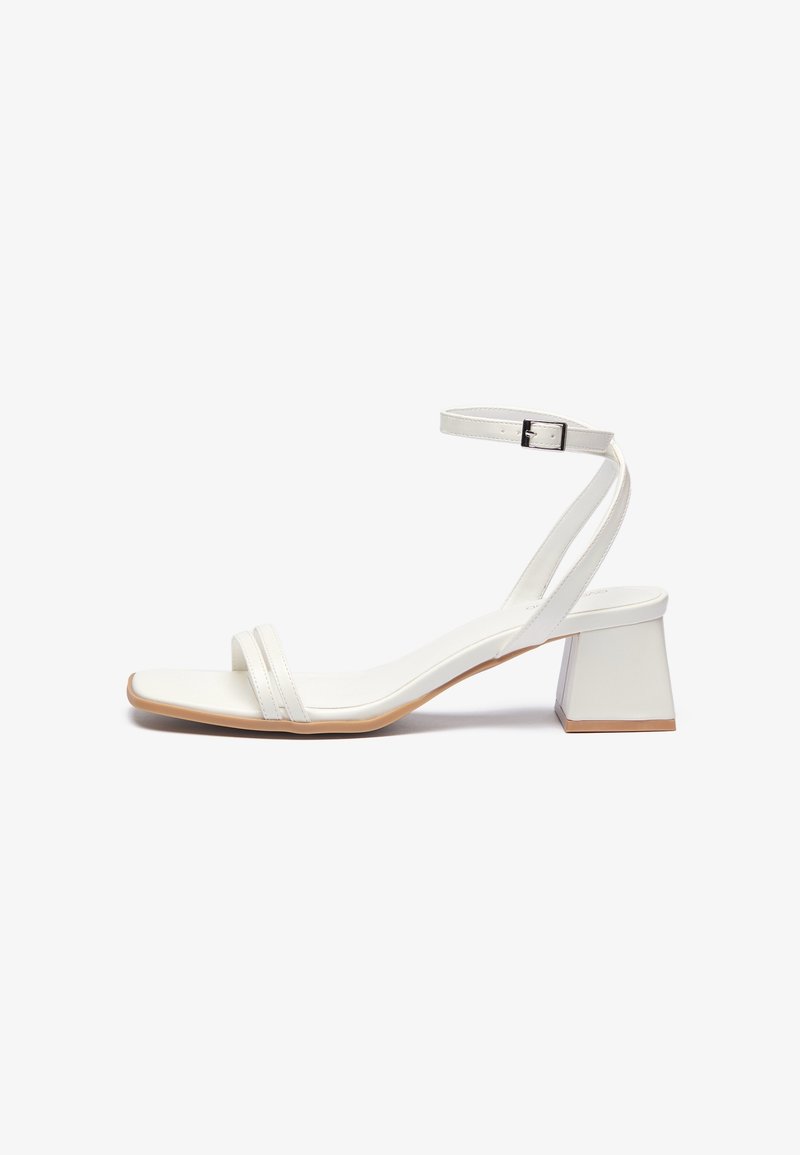 Sandale blanche à bout ouvert avec deux brides avant, brides de cheville avec boucle argentée et talon bloc sur fond blanc uni.