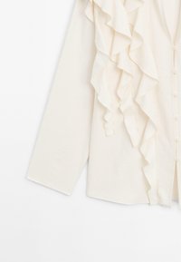 Witte blouse met lange mouwen, voorzien van een volantsdetail aan de voorkant en knoopsluiting. Gemaakt van een gestructureerde stof.