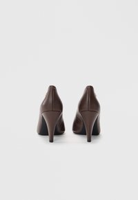 Brune lærstøvler med høj hæl og spids tå. Har en glat tekstur og en subtil gul accent på hælen.