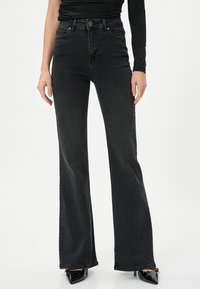 Svarta utsvängda jeans i denim med en slät textur. Har hög midja och framfickor, med subtila blekningar.