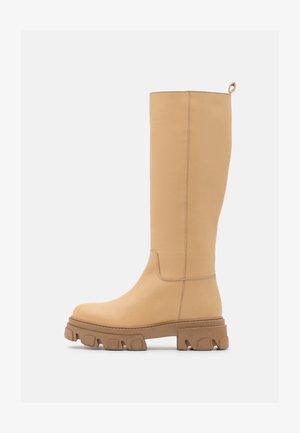 Visok bež kožni čizme s debelim potplatom i vučnom trakom na stražnjoj strani, prikazane u bočnom profilu na bijeloj pozadini.