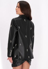 Schwarze Lederblazer mit Perlenverzierungen, klassischem Kragen und taillierter Passform, die eine glatte Textur und ein strukturiertes Design präsentiert.