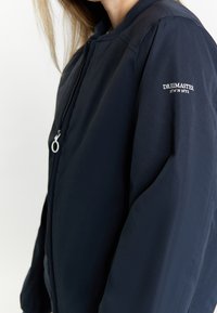 Giacca bomber navy con colletto rotondo, zip a tutta lunghezza e logo ricamato sulla manica. Tessuto liscio con una silhouette elegante.