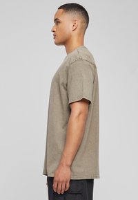 Camiseta de algodón verde oliva con mangas cortas, escote redondo y un corte holgado. Textura suave y acabado ligeramente desgastado.