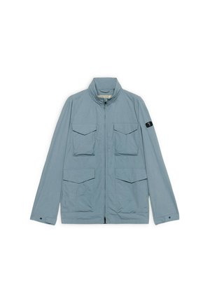 Jasnoniebieska kurtka z czterema przednimi kieszeniami na klapki, pełnym zamkiem błyskawicznym, stójką i małą czarną naszywką na lewym rękawie.