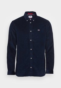 Námořnická manšestrová košile s líme�čkem na knoflíky, stříbrnými knoflíky a malou nášivkou s logem na hrudi. Má dlouhé rukávy a žebrovanou texturu.