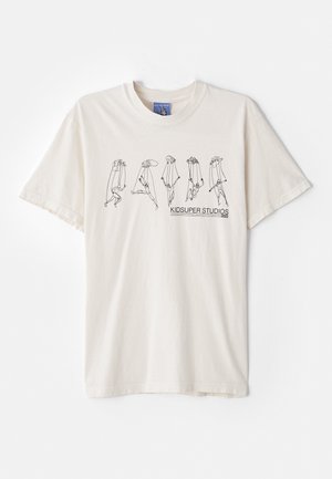 Kremowa bawełniana koszulka z krótkim rękawem, z czarnym abstrakcyjnym wzorem i napisem "KIDSUPER STUDIOS" na środku.