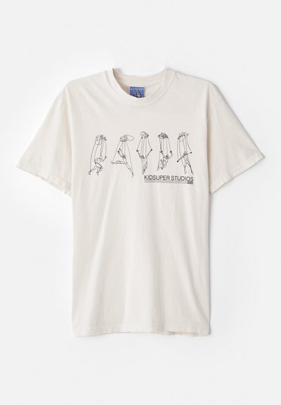Cream-colored cotton t-shirt with short sleeves, featuring a black abstract design and text “KIDSUPER STUDIOS” in the center.