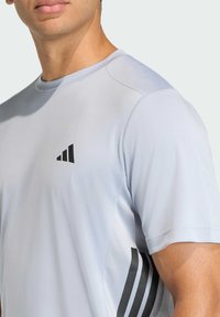 Svetlosivé športové tričko s okrúhlym výstrihom. Obsahuje čierne logo a textúrované bočné panely. Krátke rukávy a priliehavý strih.