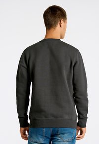 Sudadera gris oscuro de manga larga, con cuello y puños acanalados, textura suave y corte holgado. Combinada con jeans azules.