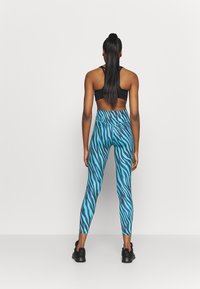Sinisiä ja mustia sebrakuosisia leggings-housuja, joissa on korkea vyötärö, valmistettu joustavasta materiaalista, yhdistetty mustan urheilutopin ja mustien lenkkareiden kanssa.