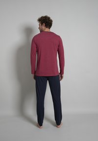 Langarmige kastanjebruine shirt met ronde hals, gecombineerd met marineblauwe broek. De stof lijkt zacht, met een ontspannen pasvorm en minimale details.