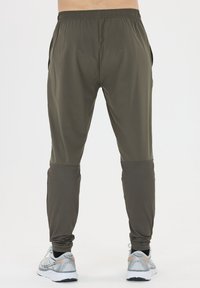 Heren sportbroeken, elastische tailleband, donkergroen, taps toelopend ontwerp met mesh accenten op de onderbenen, gecombineerd met hardloopschoenen.