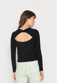 Top preto de manga longa com detalhe em forma de U nas costas. Usado com jeans verde claro, destacando um design justo e com textura.