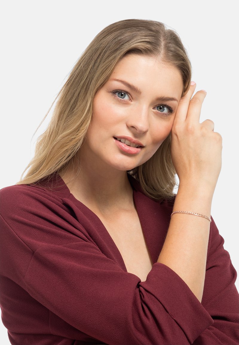 Maglietta a maniche lunghe di un profondo bordeaux con tessuto texturizzato; modello che indossa un delicato bracciale d'argento con design a catena sul polso.