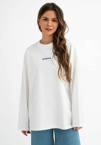 Witte oversized sweatshirt van zachte stof, met een ronde hals en lange mouwen. Aan de voorkant staat in blauwe borduursel de tekst "MIRONS."