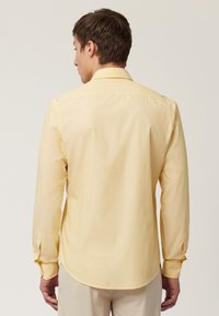 Camisa amarilla de manga larga con cuello clásico, puños abotonados y dobladillo curvado. Tela suave con una textura agradable y un diseño sencillo.