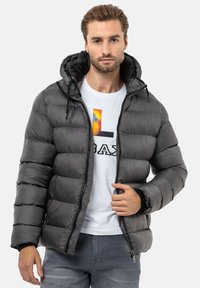Dunkelgraue Puffjacke mit gesteppter Textur, abnehmbarer Kapuze und Reißverschluss vorne. Kombiniert mit einem weißen T-Shirt mit bunten Grafiken.