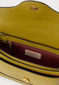 Interieur van een olijfgroene leren handtas met maroon voering, gouden rits, drukknoopsluiting en label 'Coccinelle Authentic Italian Leather'.