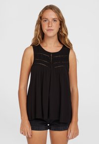 Zwarte mouwloze top met een gestructureerde schouderpartij, voorzien van horizontale borduursels en een losse snit, gecombineerd met donkere denim shorts.
