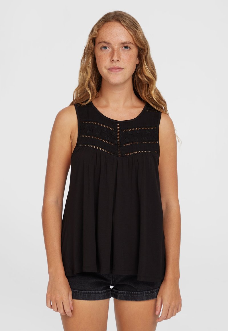 Top sin mangas negro con yugo texturizado que presenta bordados horizontales y un corte holgado, combinado con pantalones cortos de mezclilla oscuros.
