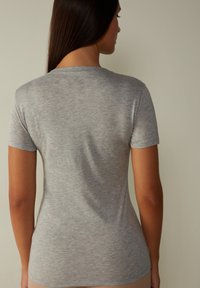 Grå kortärmad t-shirt tillverkad av mjukt, texturerat tyg. Har en rund halsringning och en åtsittande design, med en slät baksida.