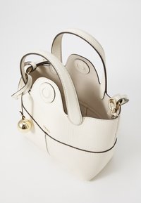 Texturiertes weißes Lederhandtasche mit runden Griffen, goldenen Beschlägen und einem dekorativen Glockenanhänger. Einfaches, strukturiertes Design mit sichtbarem Innenraum.