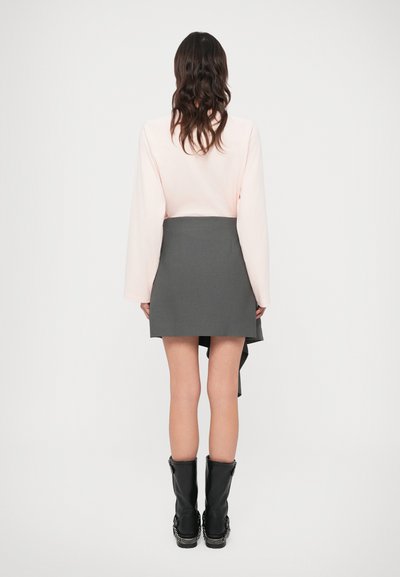 Világos rózsaszín hosszú ujjú ing, szürke aszimmetrikus szoknya, fekete térdig érő csizma, sima anyag, minimalista dizájn, látható minta vagy díszítés nélkül.