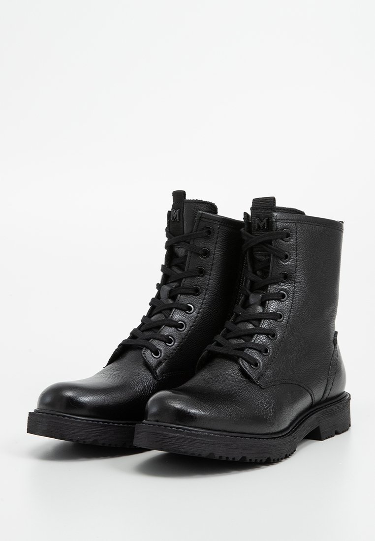Un paio di stivali alla caviglia in pelle nera con lacci, suole spesse, punte arrotondate e linguette con marchio su uno sfondo bianco.