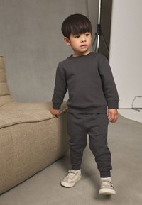 Set tamnosivih dukserice i trenirke, izrađen od mješavine pamuka. Sadrži rebraste manžete, bočne džepove i uparen je s laganim tenisicama.