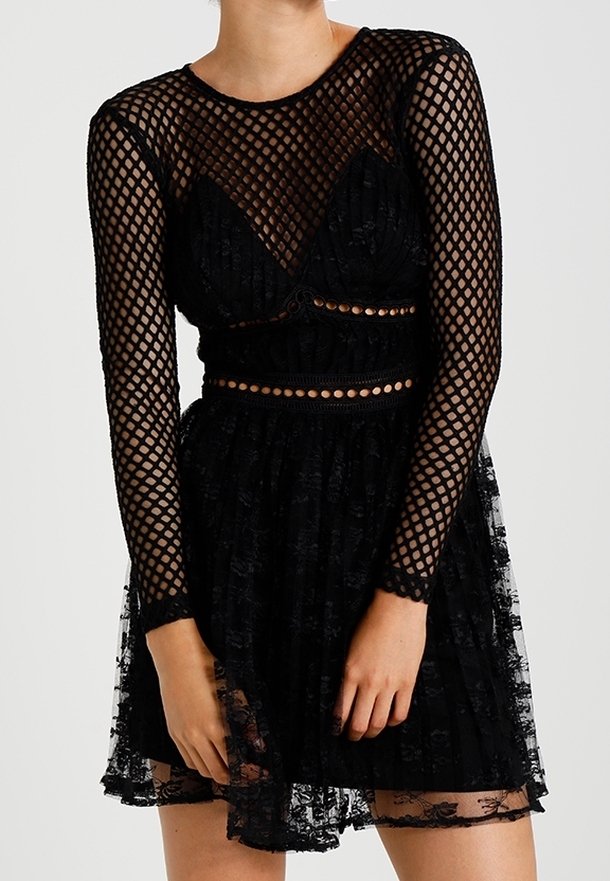 Femme portant une robe en dentelle noire avec des manches longues en maille et des découpes circulaires à la taille.