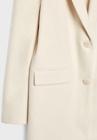 Cappotto in misto lana color crema con colletto a revers, design monopetto, due bottoni e tasca con patta sul lato sinistro.